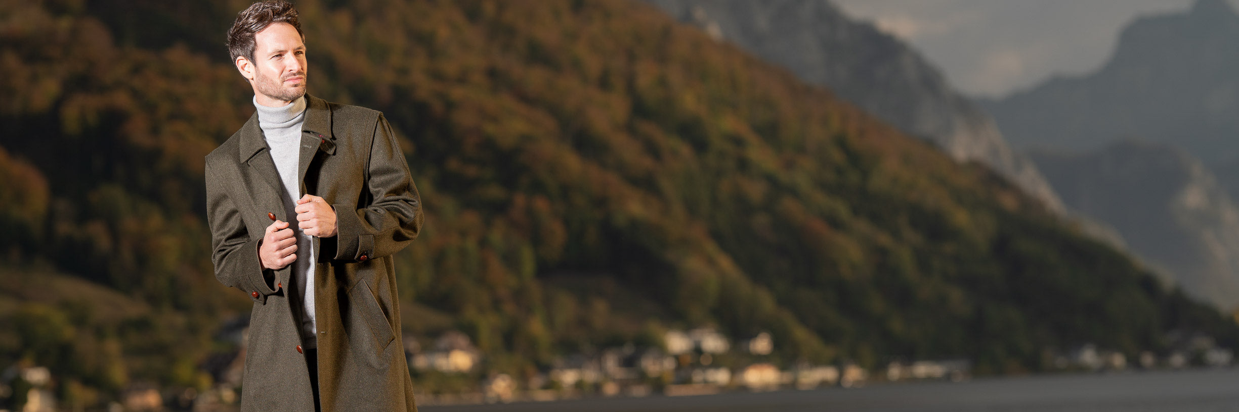 young man wearing austrian hunting loden coat with lake and mountains in background