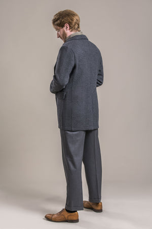 a side backside view of a 30 year old man wearing a 100% virgin austrian loden wool coat over a loden wool vest and loden wool pants