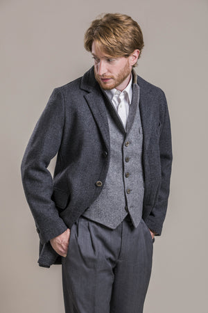 a frontal view of a 30 year old man looking away from the camera wearing a 100% virgin austrian loden wool coat over a loden wool vest and loden wool pants